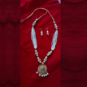Traditional white beaded necklace set with antique gold round pendant and matching earrings on a red velvet background.